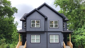 A two-story house with a dark exterior, a front porch with wooden steps, and a driveway leading to the entrance. - Luxurious 8 bd/6ba with ROOFTOP! Price is the total! (Nashville)