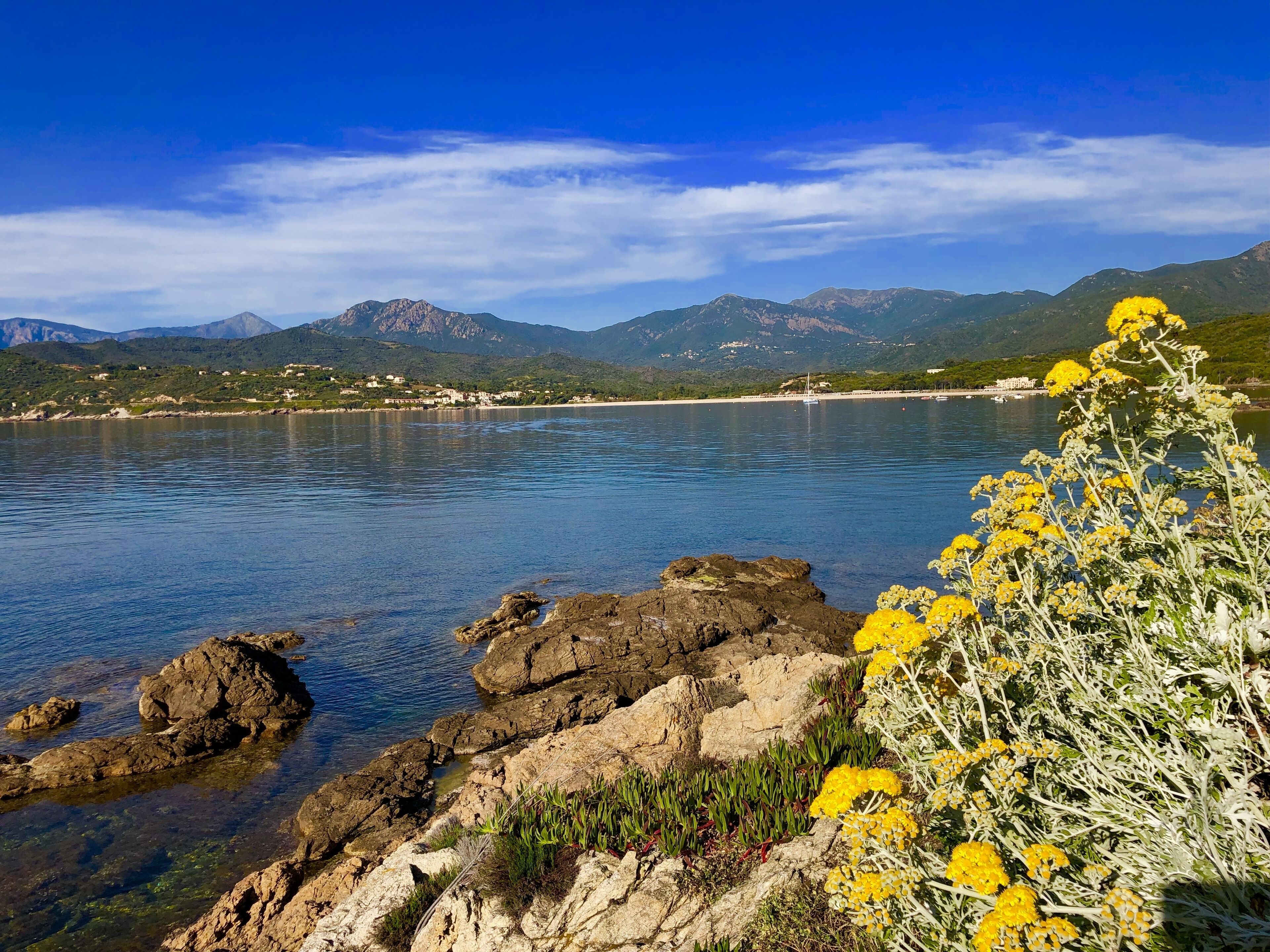 A coastal landscape with rocky shores, clear water, and distant mountains.