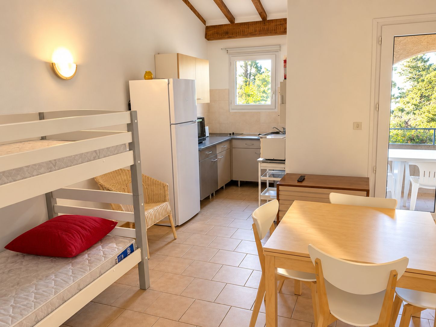 A compact room with bunk beds, a kitchenette, a dining table, and a window with a view of trees.
