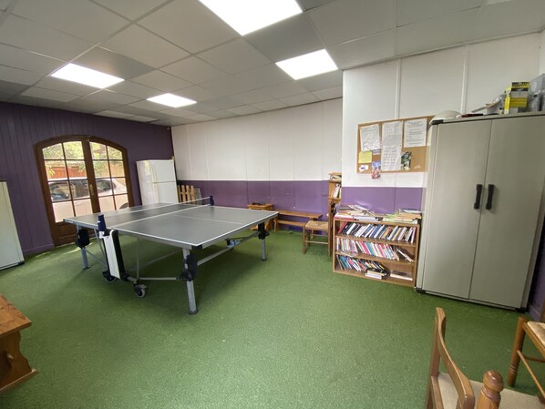 A room with a ping pong table, a bookshelf, a cabinet, and a door with a view of the outside.