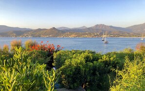 A coastal landscape with a clear view of the sea, boats, and distant mountains.