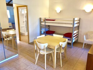 Une pièce avec un lit superposé, une table en bois avec des chaises, une chaise blanche et une petite table blanche.