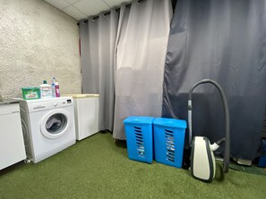 A laundry area with a washing machine, detergent bottles, and a vacuum cleaner.