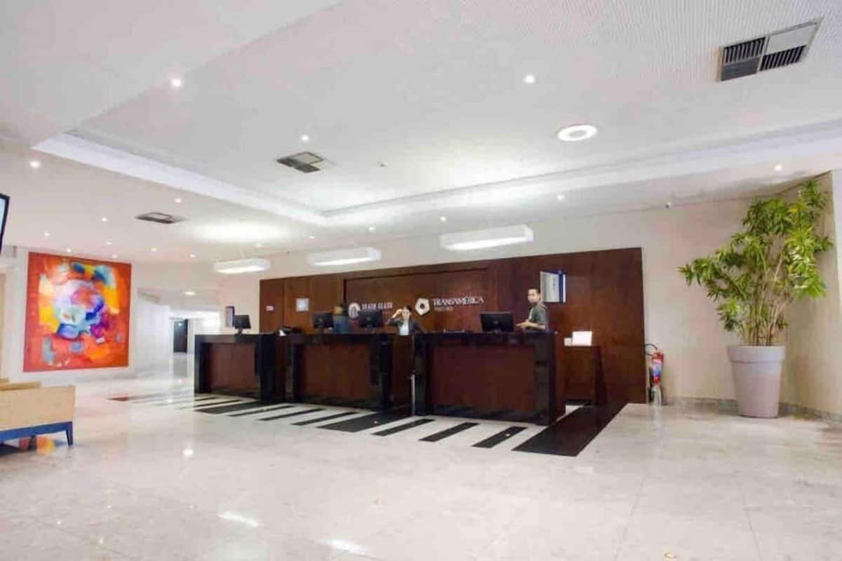 A reception desk with a sign reading 'TRANSAVENTICA,' a large abstract painting on the wall, and a potted plant to the right.