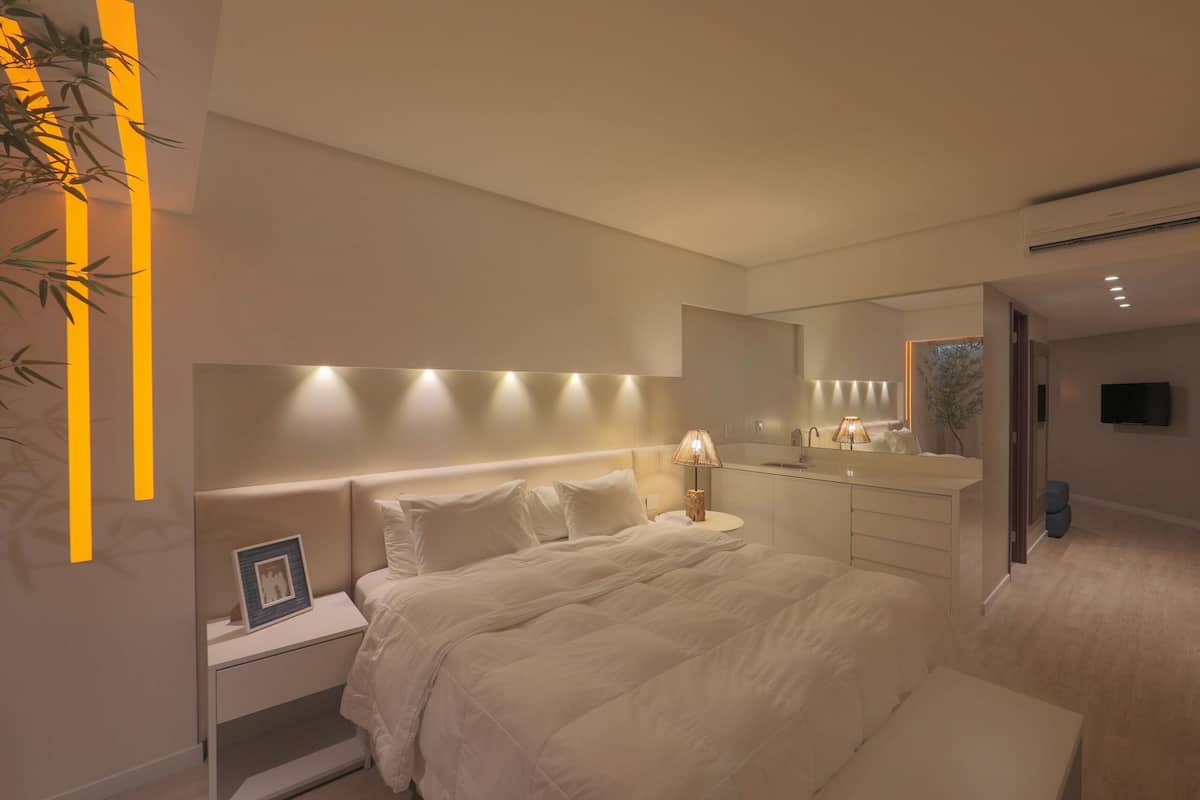 A modern bedroom with a bed, bedside table, lamp, and a mirror.