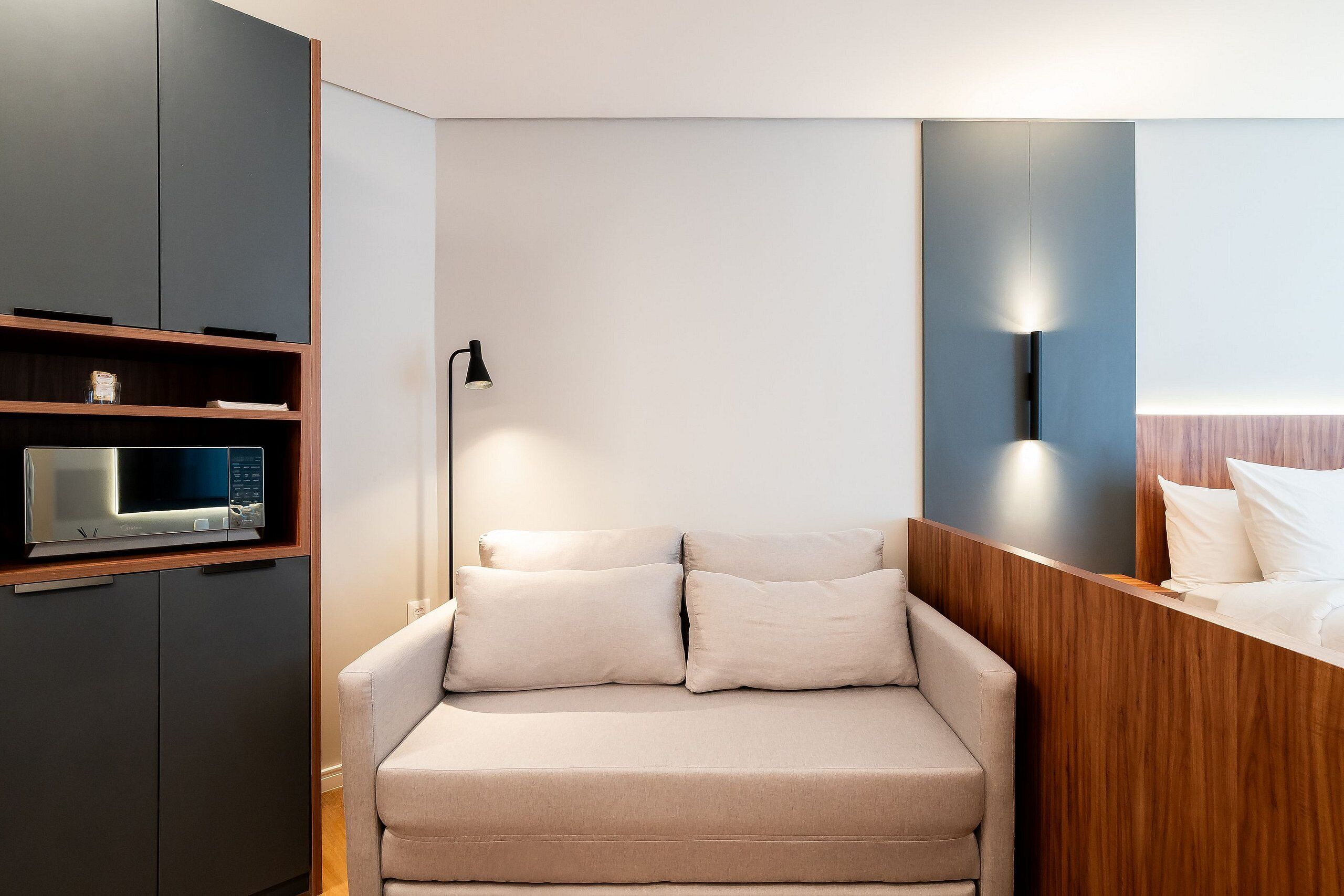 Habitación de hotel moderna con sofá, televisor de pantalla plana, lámpara y aplique de pared.