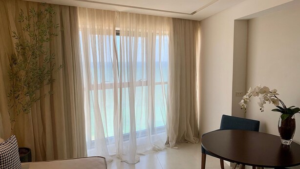 A room with sheer curtains, a dining table, chairs, a vase with flowers, and a potted plant. - HY Beach Flats - International (Recife)