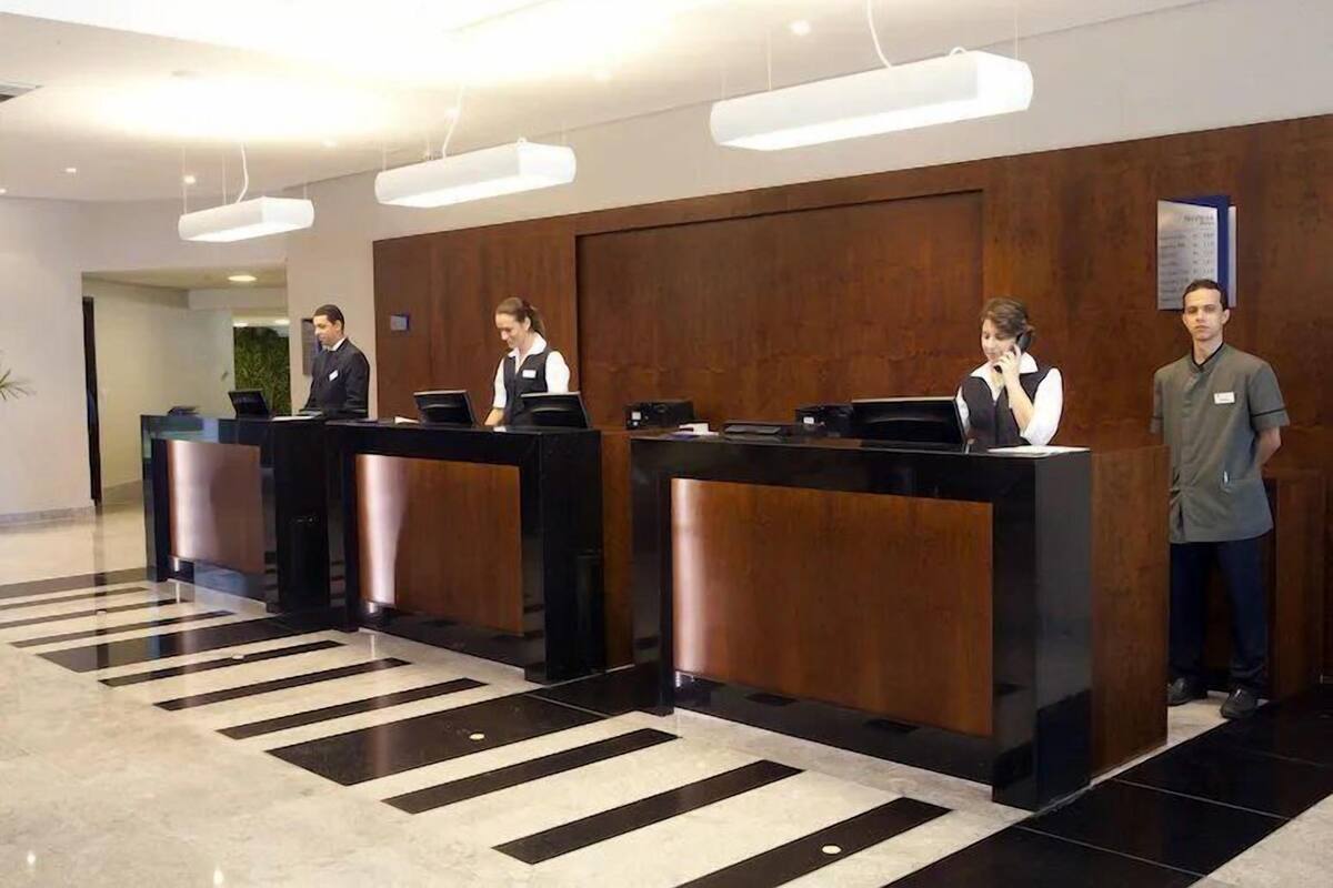 A reception area with three receptionists at counters, a wooden wall, and a black and white striped floor.