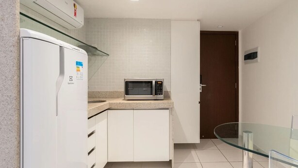 A compact kitchen with a refrigerator, microwave, and a glass table. - HY Beach Flats - International (Recife)