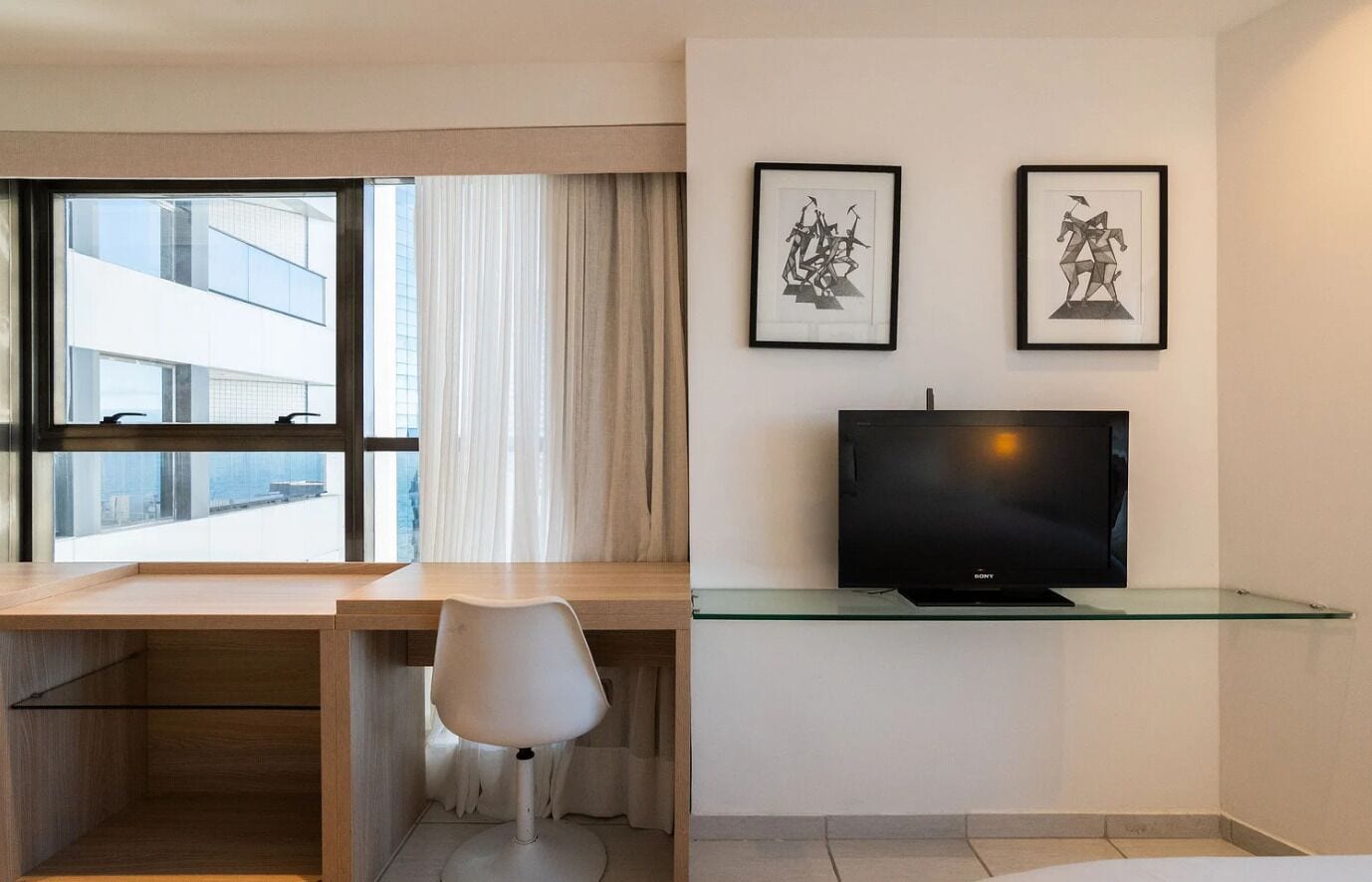 A hotel room with a desk, chair, TV, and two framed pictures on the wall.