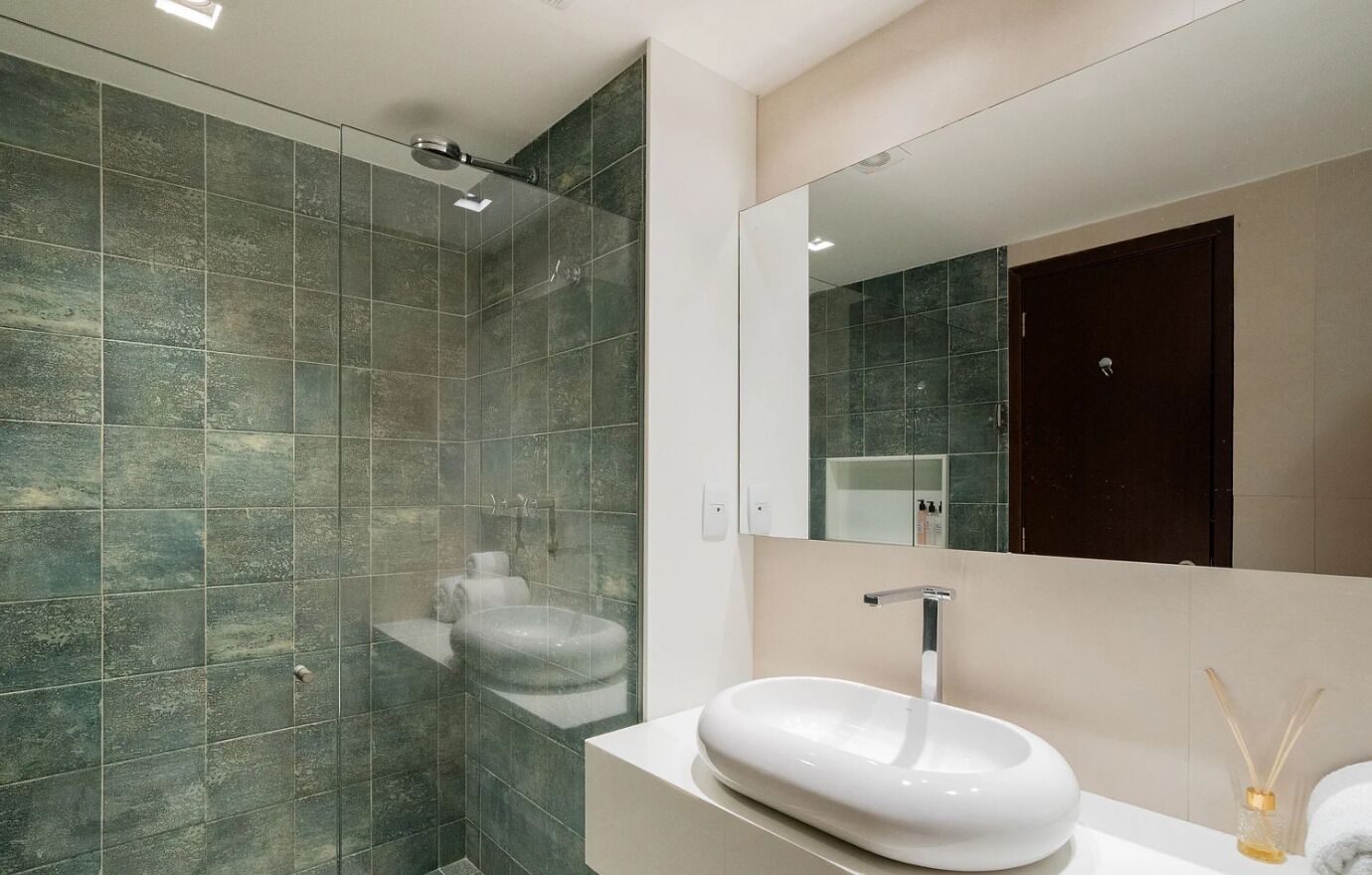 Un baño moderno con ducha de vidrio, un lavabo blanco y un espejo grande.