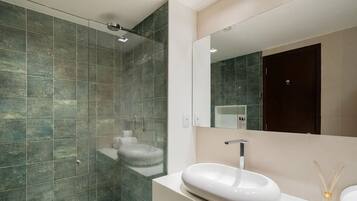 Un baño moderno con ducha de vidrio, un lavabo blanco y un espejo grande.