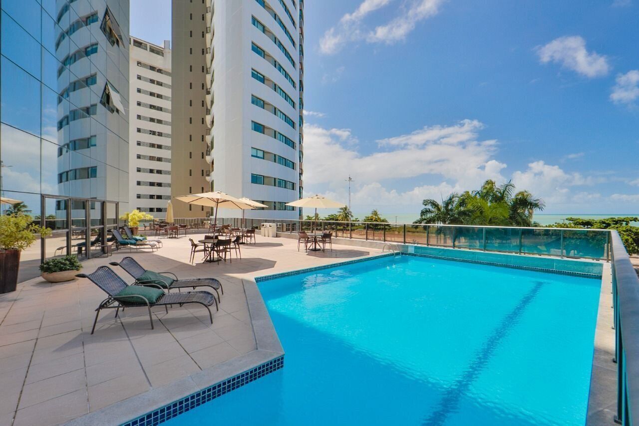 Piscina no terraço com espreguiçadeiras e guarda-sóis, cercada por edifícios altos.