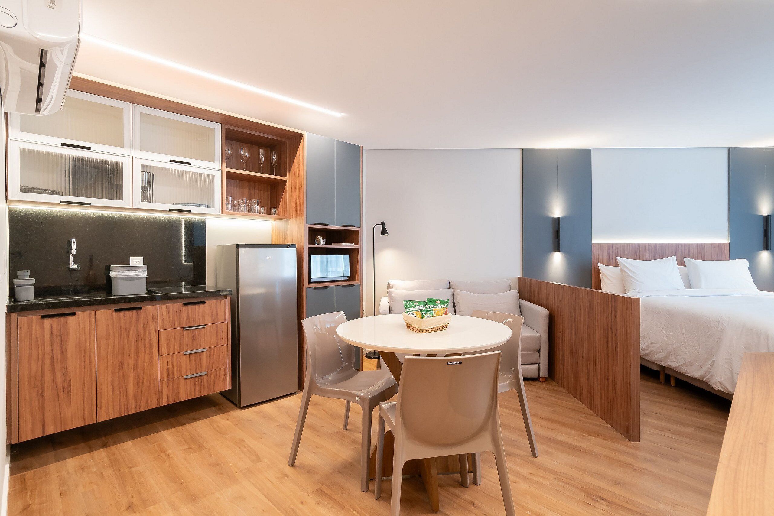 A compact hotel room with a kitchenette, a dining area, and a bed.
