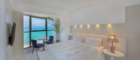 A bedroom with a large bed, a bedside table with a lamp, a chair, a small table, and a TV.