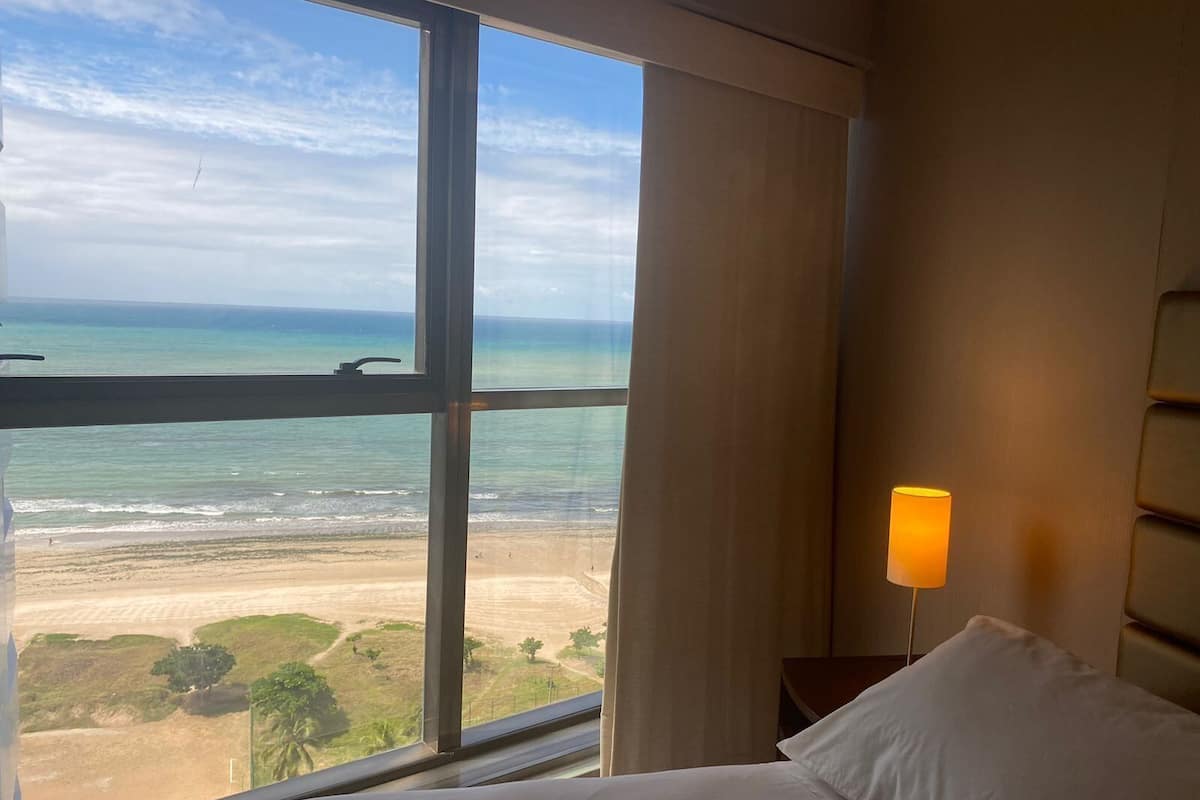 A hotel room with a large window overlooking a beach and ocean.