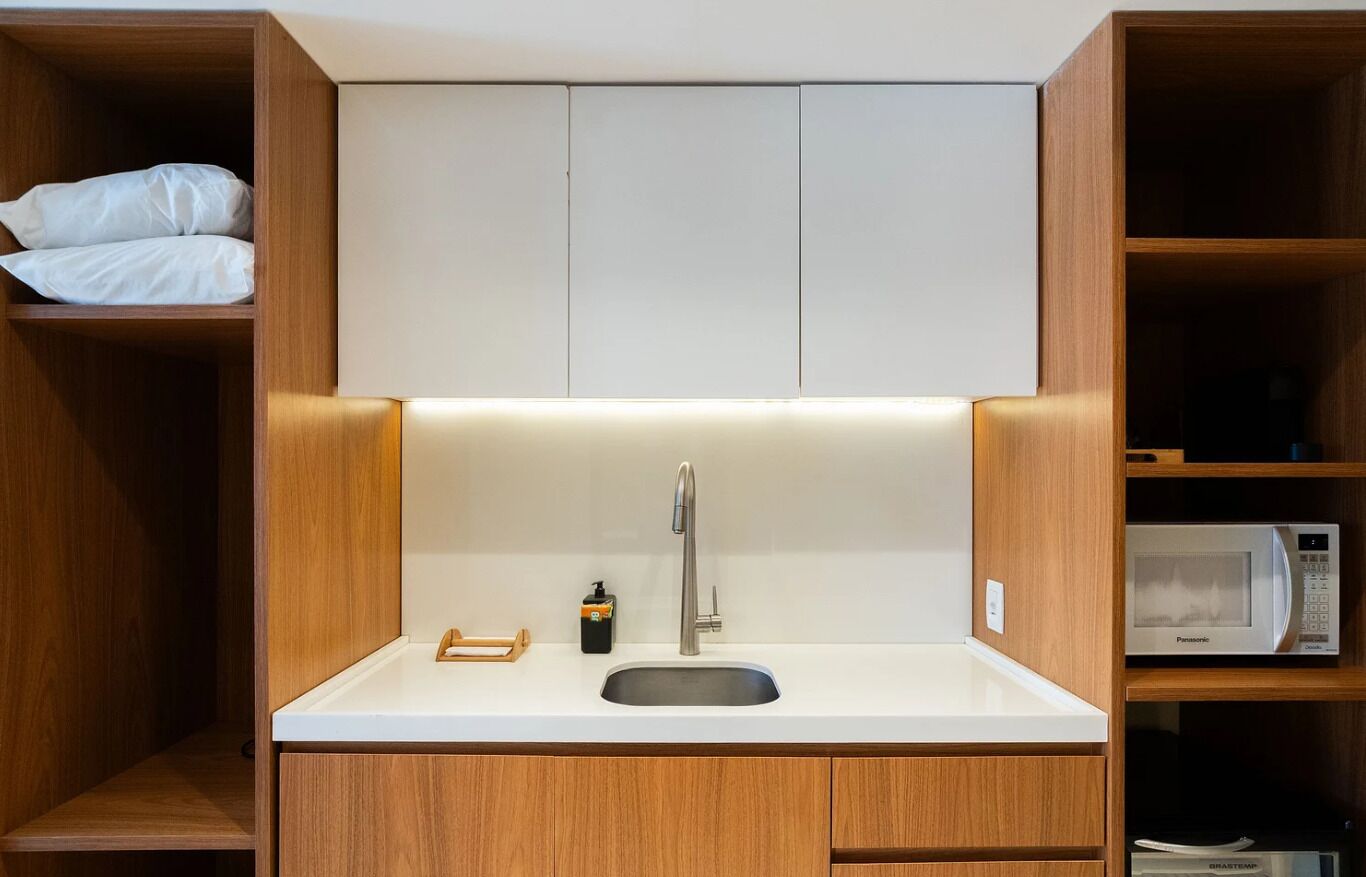 Cocina compacta con pileta integrada, muebles de madera y un microondas.