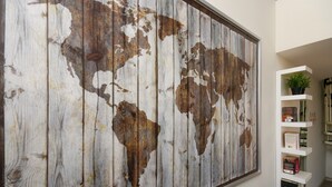 Eine große Weltkarte an einer Wand, neben einem weißen Bücherregal mit Büchern und einem Topfpflanzen.
