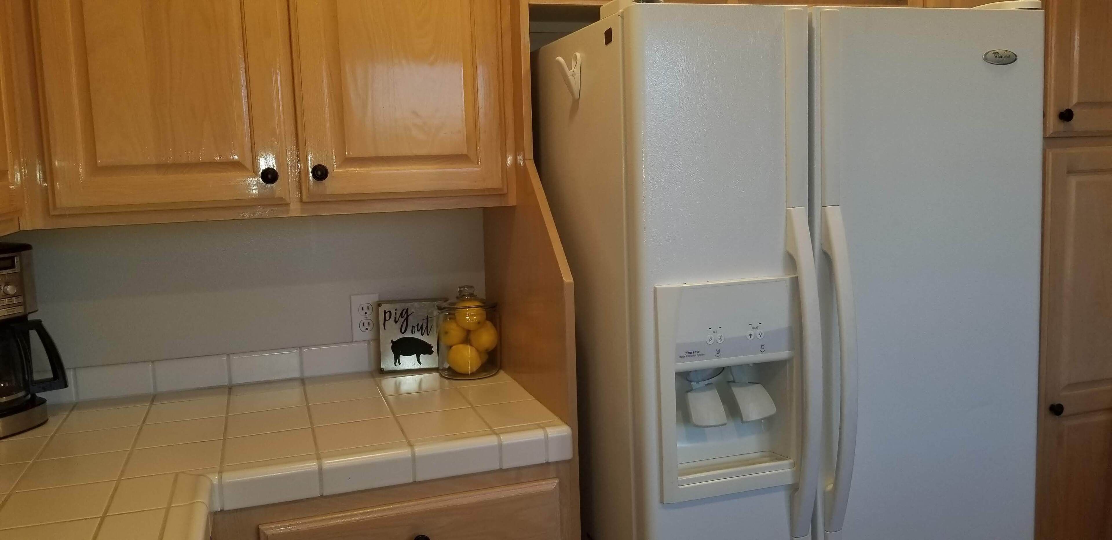 A kitchen with wooden cabinets, a white refrigerator, a countertop with a toaster, and a jar of lemons.