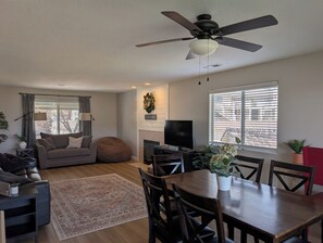 A living room with a sofa, a dining table with chairs, a ceiling fan, a TV, and a fireplace.
