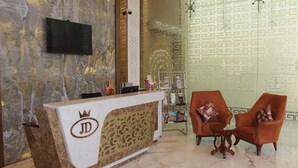 Uma área de recepção com piso de mármore, balcão de atendimento com logotipo, duas poltronas, uma mesa pequena e uma estante decorativa.