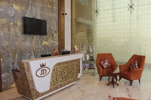Un área de recepción con piso de mármol, una mesa de recepción con un logotipo, dos sillones, una mesita y una estantería decorativa.