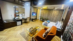 Quarto de hotel compacto com sofá, mesinha de centro, televisão, escrivaninha com cadeira e cama com travesseiro.