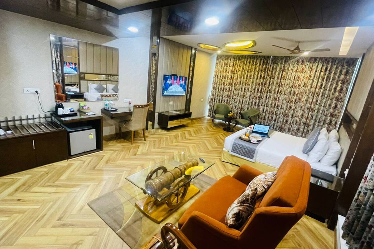 A compact hotel room with a sofa, a small coffee table, a TV, a desk with a chair, and a bed with a pillow.