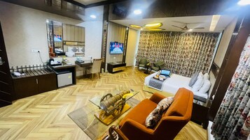Habitación de hotel compacta con sofá, una mesita de centro pequeña, televisor, escritorio con silla y cama con almohada.