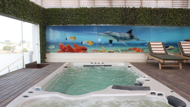 Uma banheira de hidromassagem com um mural da vida marinha, cercada por um deck de madeira e espreguiçadeiras.