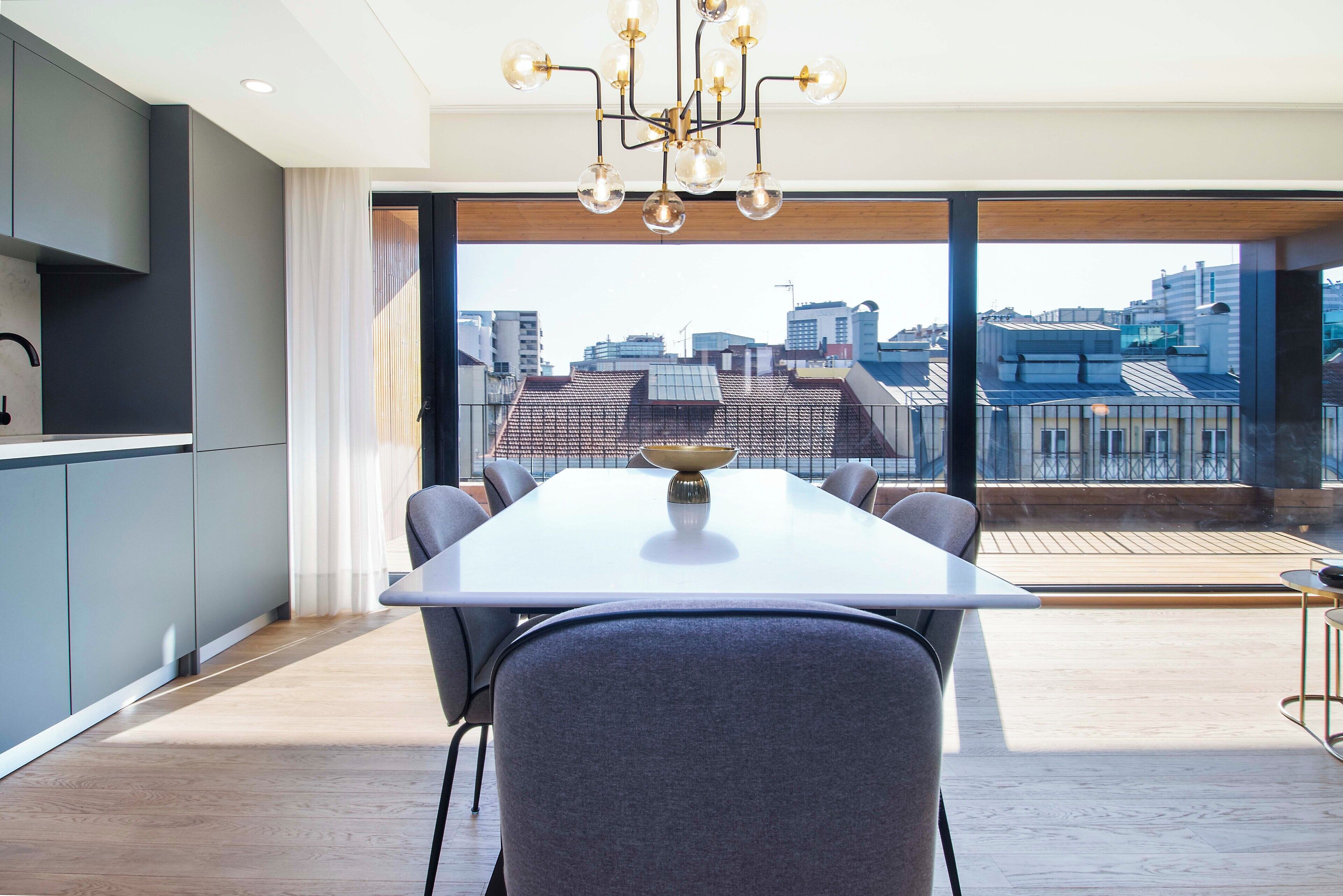 Un espace de restauration moderne avec une grande table, des chaises grises et une vue sur la ville grâce à de larges fenêtres.