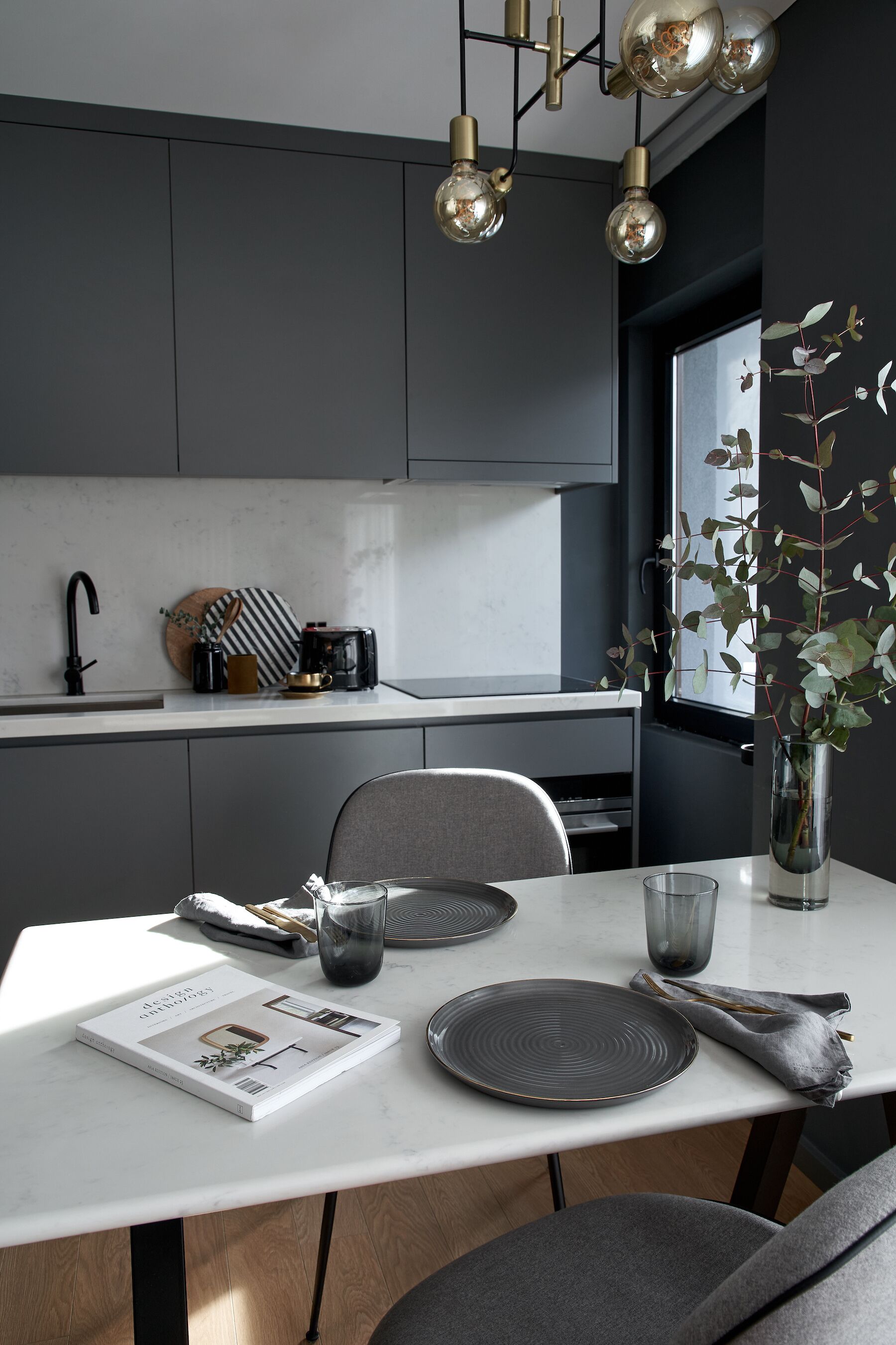 Een moderne keuken met donkere kastjes, een wit aanrechtblad en een eethoek met een tafel gedekt voor twee personen.