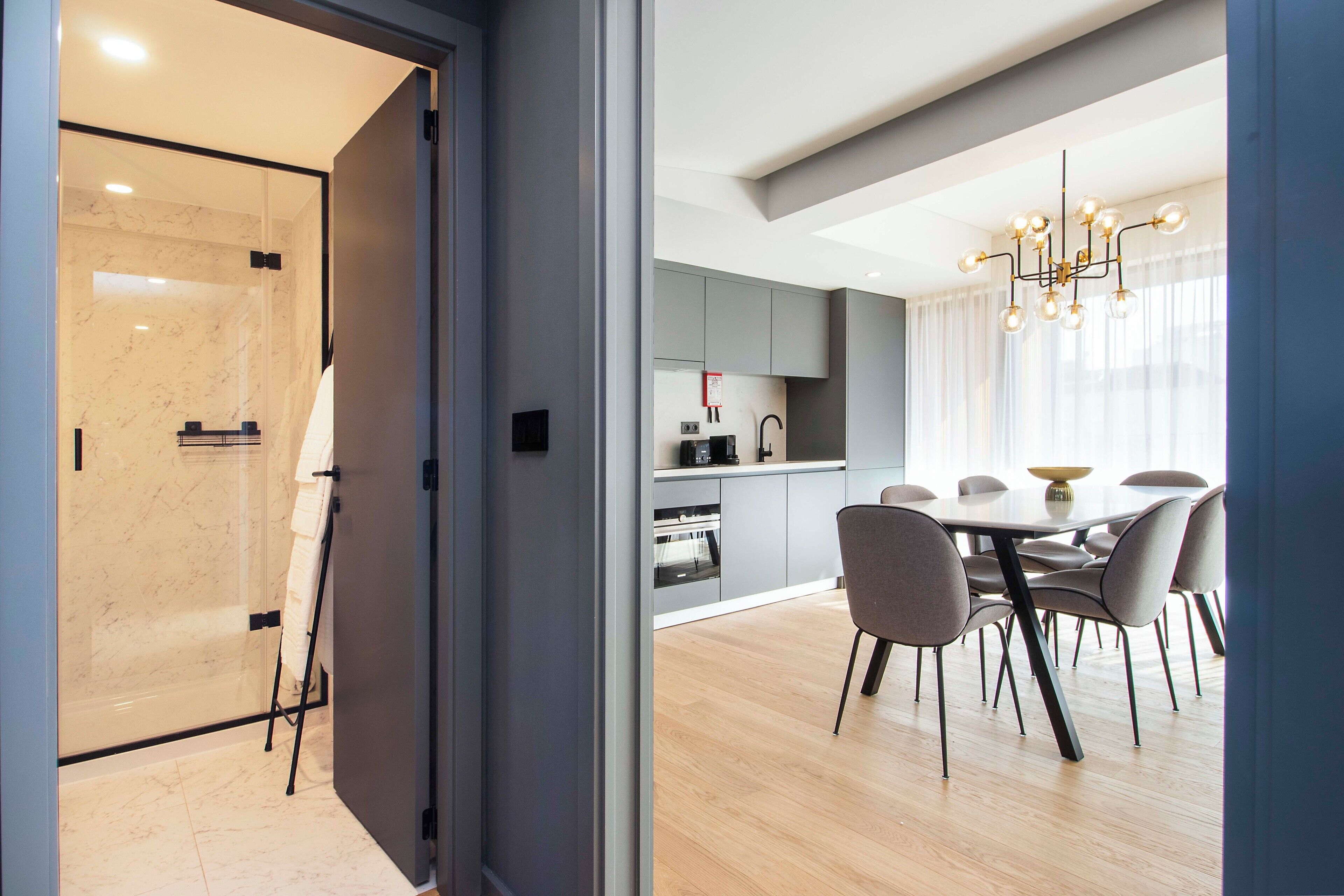 Una cocina moderna con armarios grises, un área de comedor con una mesa redonda y sillas, y una cabina de ducha de vidrio.