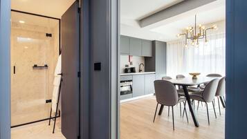 Una cocina moderna con armarios grises, un área de comedor con una mesa redonda y sillas, y una cabina de ducha de vidrio.