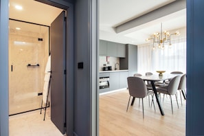 Una cocina moderna con armarios grises, un área de comedor con una mesa redonda y sillas, y una cabina de ducha de vidrio.