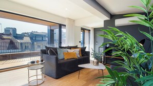 Ein modernes Wohnzimmer mit großem Fenster, einer Couch, einem Couchtisch und einem Blumentopf.