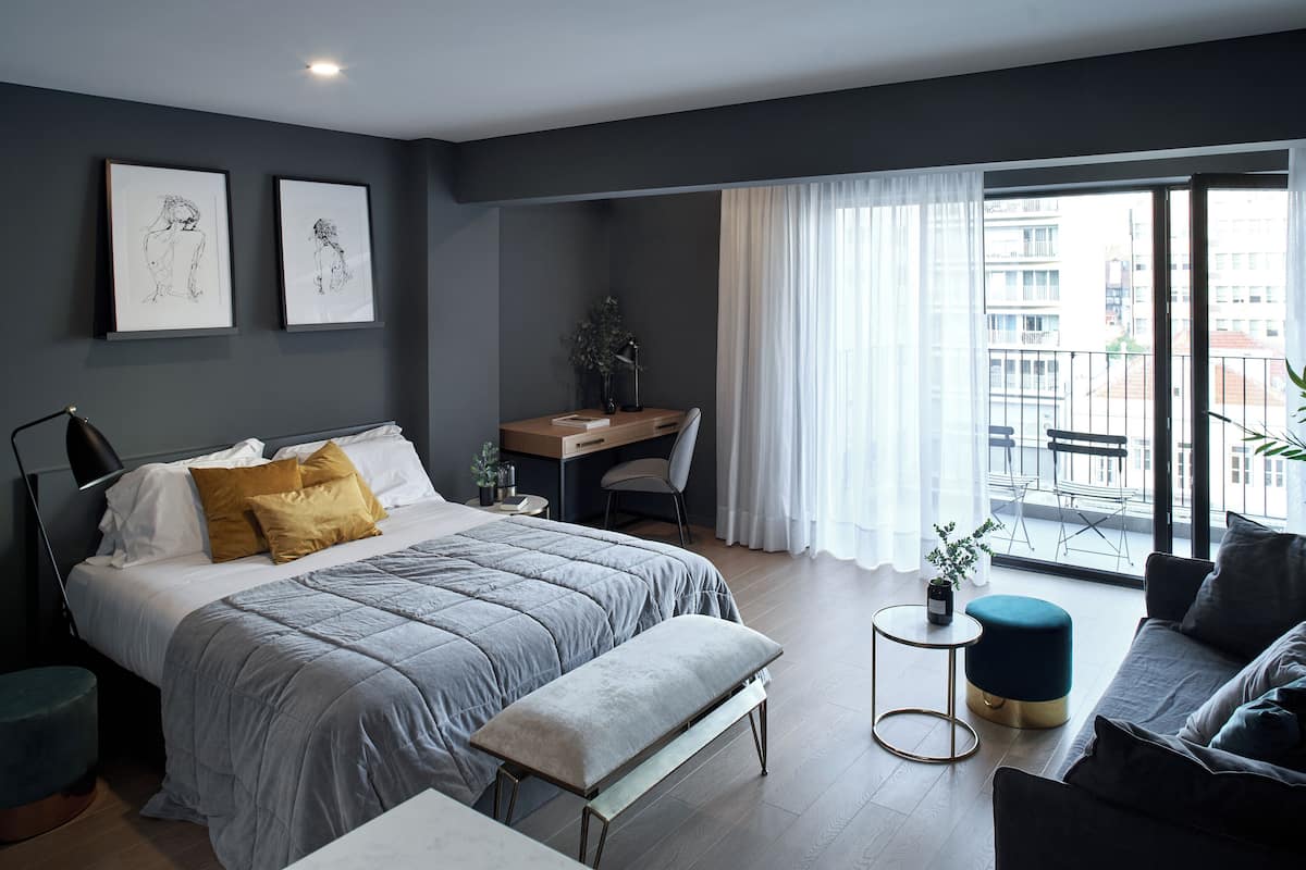Un dormitorio moderno con una cama grande, un escritorio y un balcón con vistas a la ciudad.