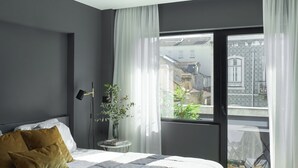 Ein modernes Schlafzimmer mit einem großen Bett, einem Nachttisch, einem Sessel und Blick auf den Balkon.