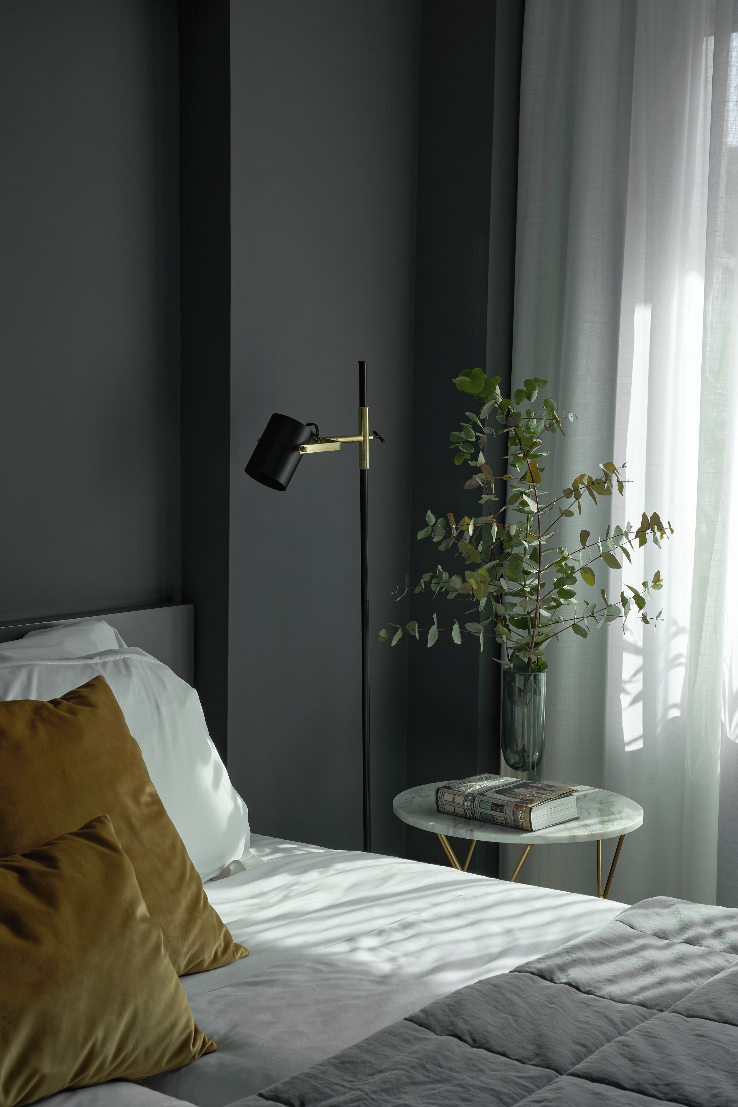 Ein Schlafzimmer mit einem Bett, einem Nachttisch mit einem Buch, einer Stehlampe und einer Topfpflanze.