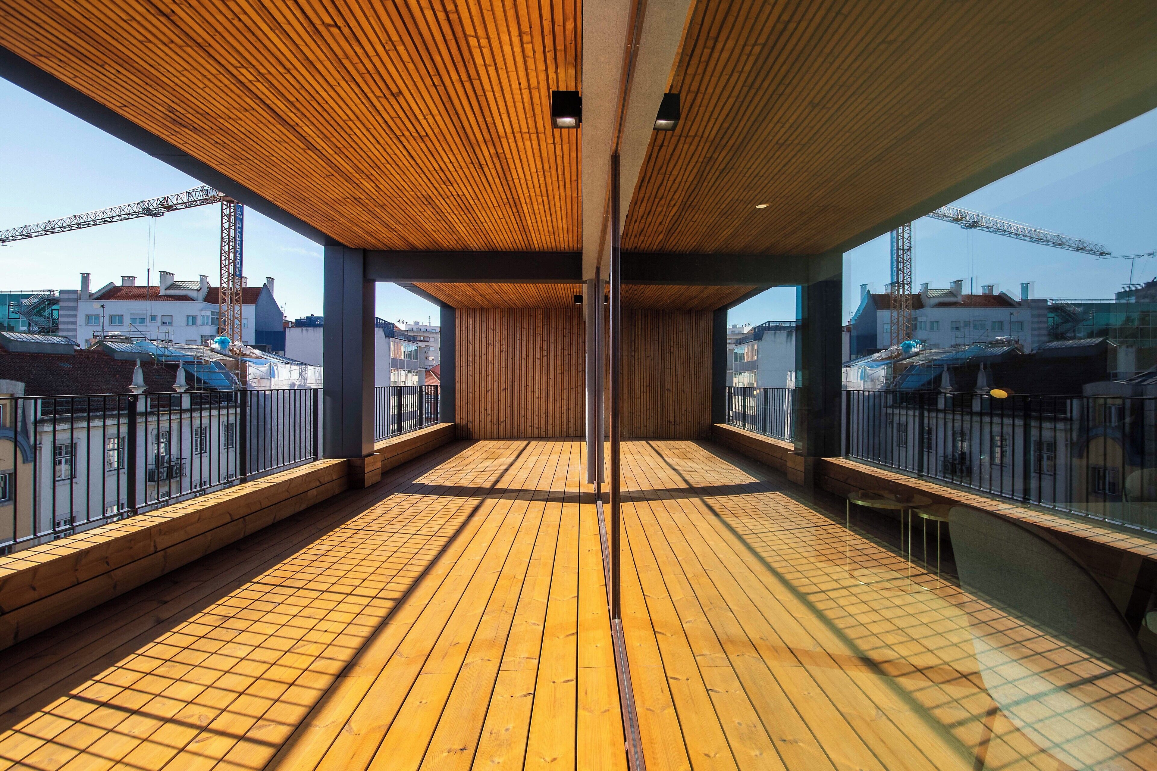 A spacious balcony with wooden flooring, metal railings, and a view of construction cranes in the background.