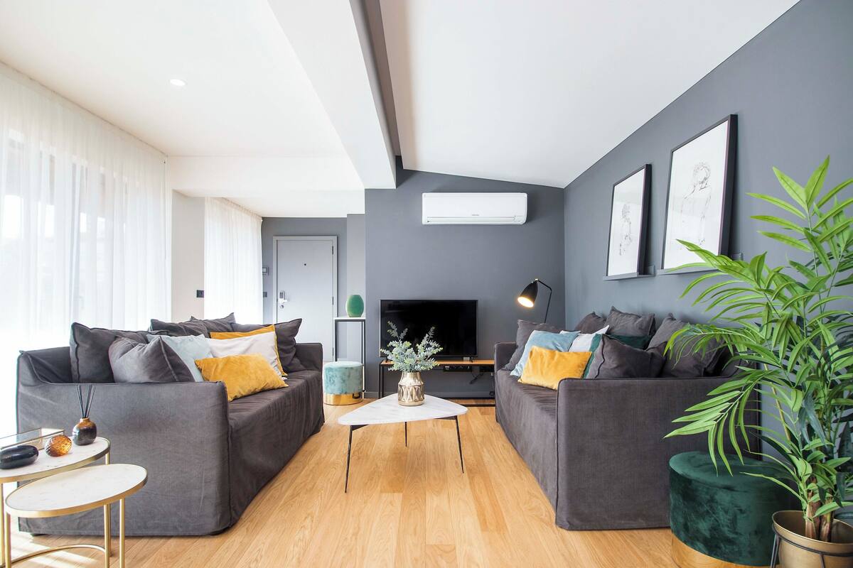 Una sala de estar moderna con dos sofás grises, una mesa de centro blanca y una planta verde grande.
