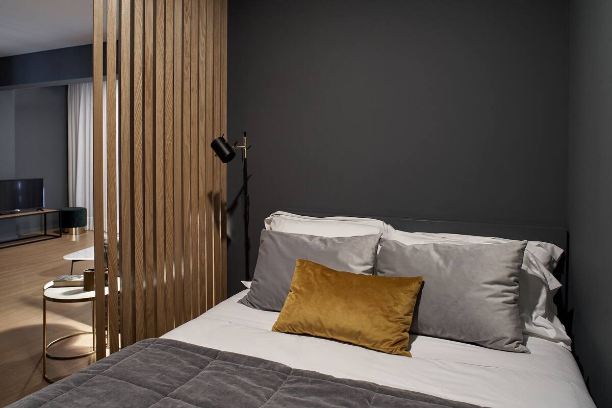 Un dormitorio moderno con una cama, una mesita de noche, una lámpara y un televisor al fondo.