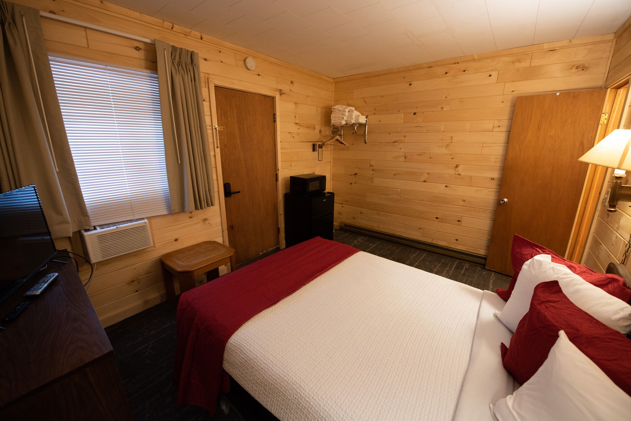Una habitación con paneles de madera, una cama, un escritorio, un calentador y una lámpara.