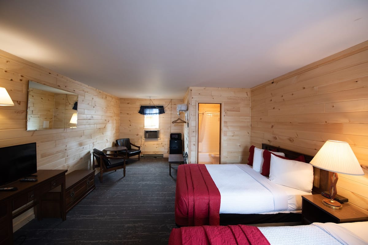 A wooden room with a bed, a desk, a chair, a TV, and a mirror.