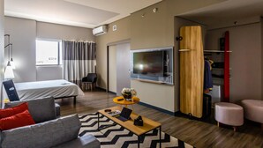 Una habitación de hotel moderna con cama, sofá, mesa de centro, televisor y armario.