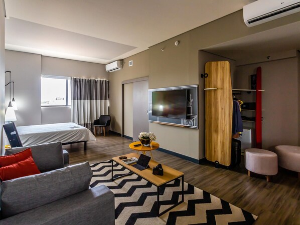 Moderni hotellihuone, jossa on sänky, sohva, sohvapöytä, televisio ja vaatekaappi.