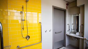 A bathroom with yellow tiled walls, a shower area, a sink, and a door.
