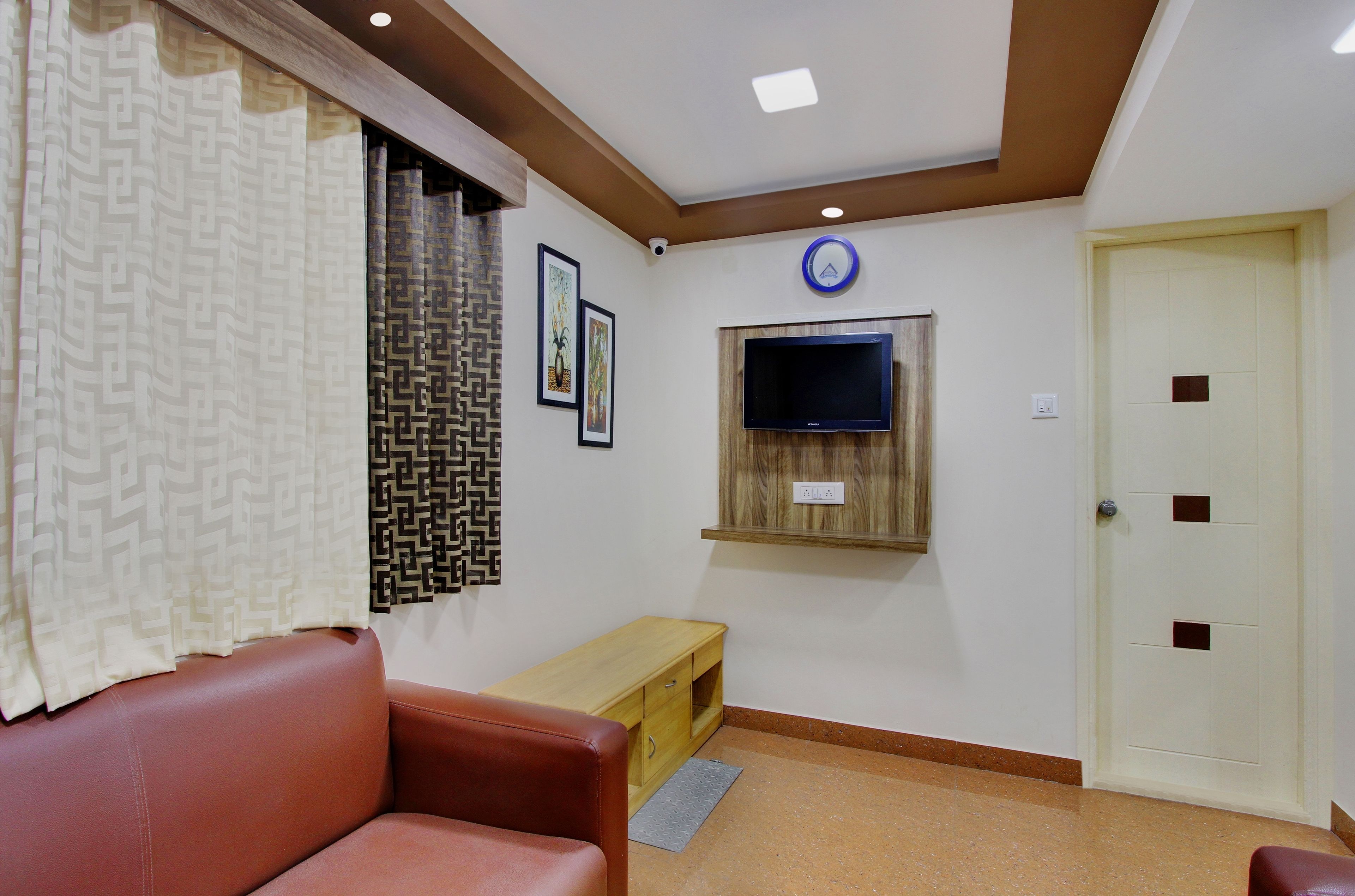 A room with a brown leather sofa, a wooden bench, a television mounted on the wall, and a door with a handle.