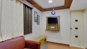 A room with a brown leather sofa, a wooden bench, a television mounted on the wall, and a door with a handle.