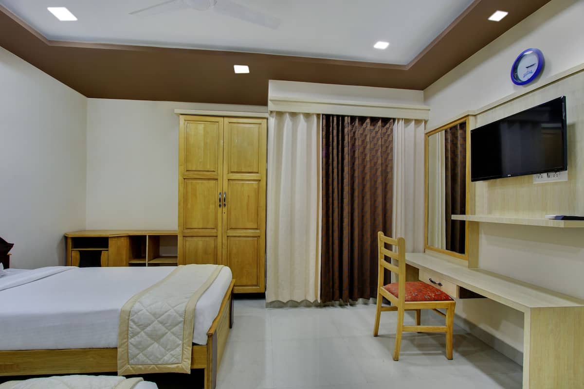 A hotel room with a bed, a desk with a chair, a TV, and a wardrobe.